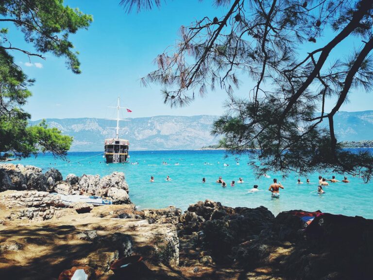 Beautiful beach scene with swimmers and a boat near rugged coastline under clear blue skies.