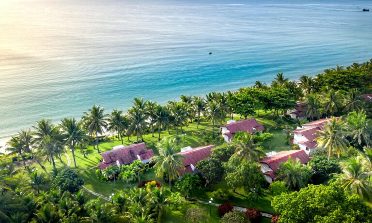 Drone shot of tropical beachside resort with palm trees and ocean view.