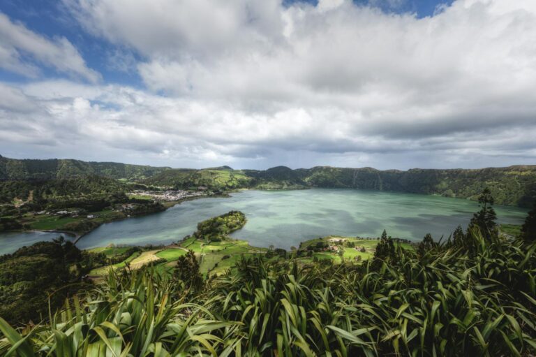 A stunning view of the Lagoa das Sete Cidades, surrounded by lush greenery under a cloudy sky.