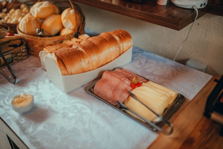 A delightful continental breakfast setup featuring sliced bread, ham, cheese, and rolls on a linen-covered table.