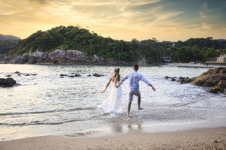 A couple joyfully walks along the shore at sunset, embracing romance by the sea.