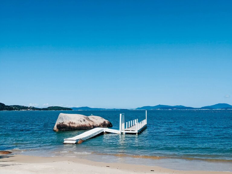 Peaceful beachfront with wooden dock, blue sky, and serene sea.