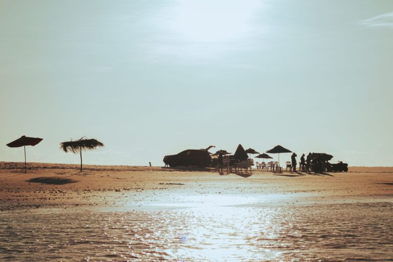A tranquil beach scene in João Pessoa, Brazil at sunset with silhouetted people and parasols.