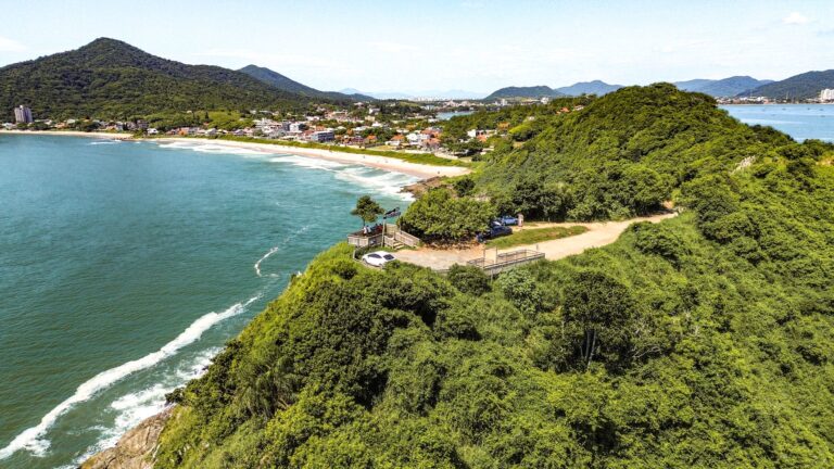 Aerial view of Itajaí coastline with lush green hills and blue ocean under a clear sky.