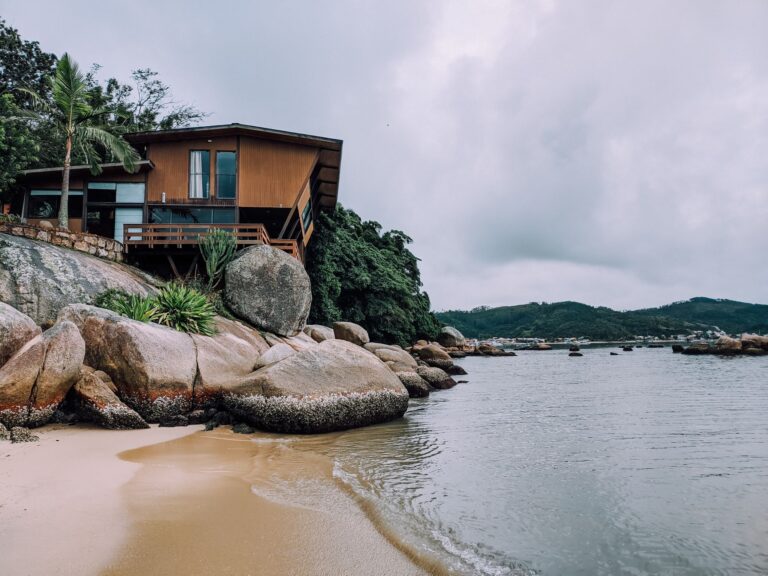 A modern wooden house perched on rocky coastline with serene ocean views.