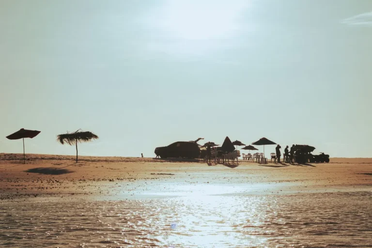 A tranquil beach scene in João Pessoa, Brazil at sunset with silhouetted people and parasols.