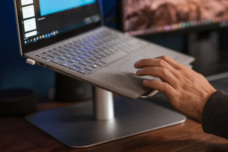 Crop unrecognizable male browsing modern netbook and scrolling touchpad placed on stand on desk